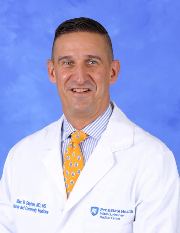 Doctor in white coat and yellow tie smiling.