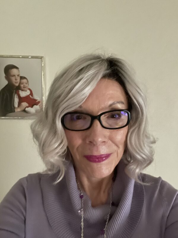 Woman with gray hair and glasses smiling indoors.