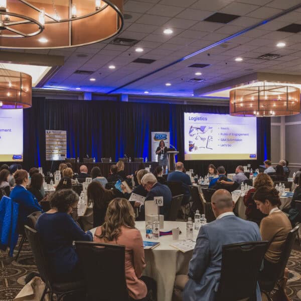 Conference presentation with audience and large screens.