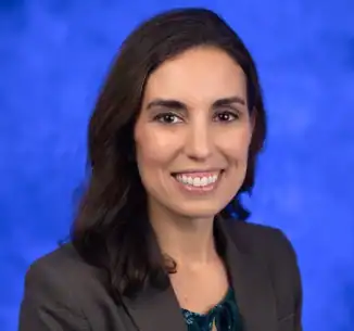 Smiling woman in business attire, blue background.